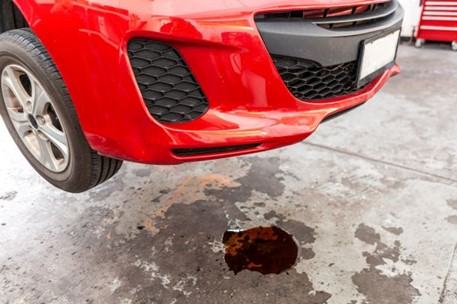 Oil drips onto the floor of an auto shop from a car with a leak emphasizing the importance of knowing the causes, warning signs, and solutions for oil leaks in your car.