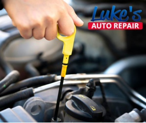 A person pulling out the oil dipstick to check its levels. The Luke’s Auto Repair logo is displayed
in the top right corner of the image. 